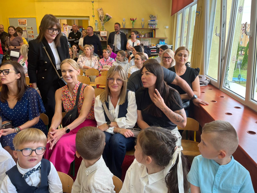 Sala wypełniona jest dorosłymi i dziećmi. W pierwszych rzędach siedzą rodzice rozmawiający ze sobą