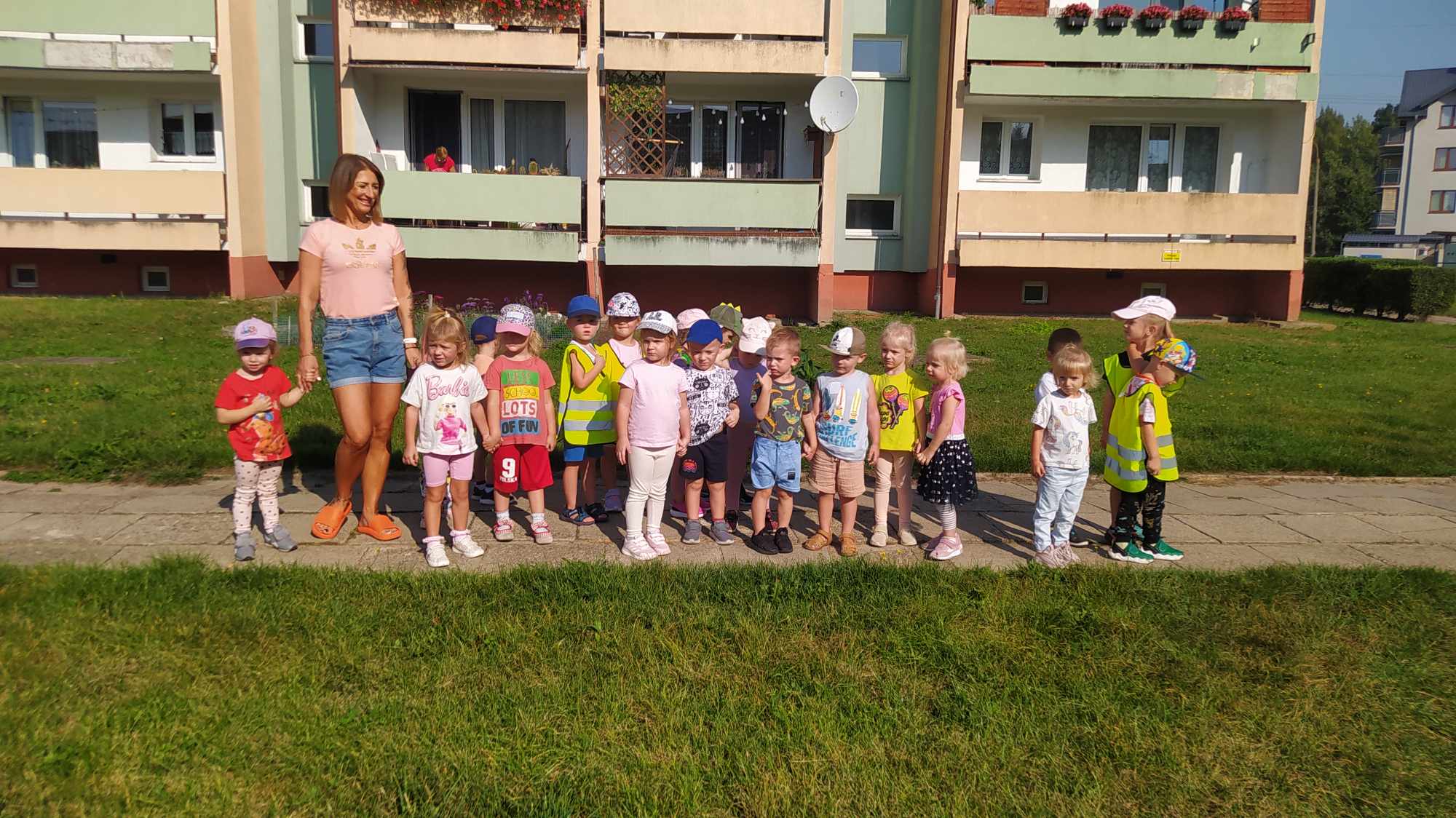 grupa dzieci stojąca na chodniku na tle bloku mieszkalnego