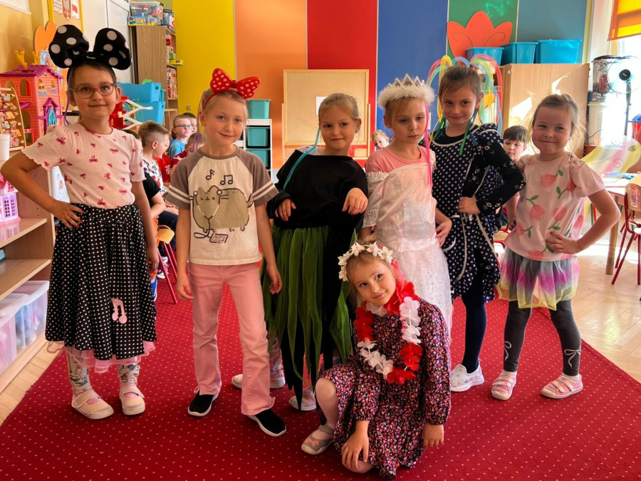 Grupa dziewczynek pozuje w kolorowych przebraniach. Wśród strojów widać między innymi suknię księżniczki spódniczkę hawajską skrzydełka wróżki oraz opaski z dużymi kokardami i uszami