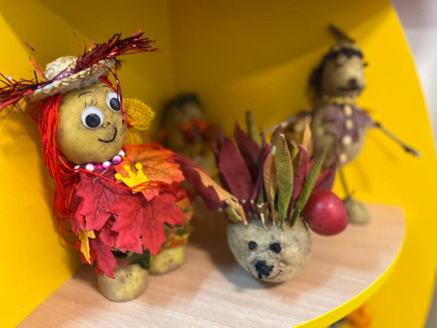 Prace plastyczne wykonane z ziemniaków. Na pierwszym planie znajduje się postać z czerwonymi włosami z włóczki w kapeluszu i sukience z kolorowych liści ozdobiona naszyjnikiem z koralików