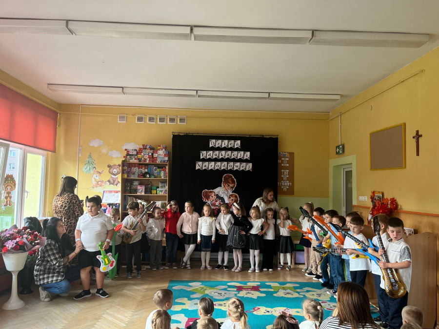 Dzieci prezentują występ muzyczny z wykorzystaniem zabawkowych gitar przed publicznością podczas obchodów Dnia Edukacji Narodowej