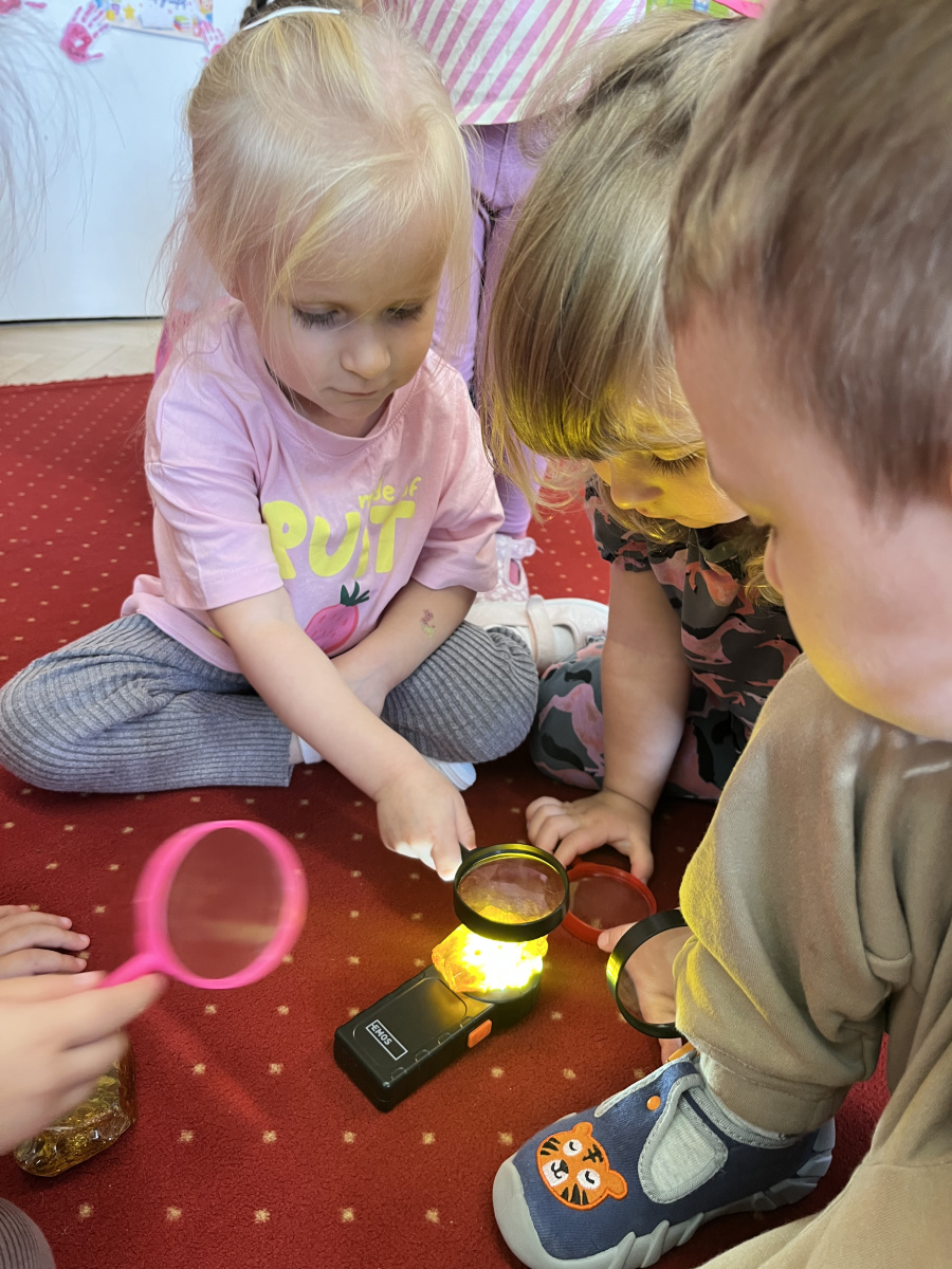 Dzieci oglądają bursztyn podświetlony latarką i obserwują go przez lupy podczas zajęć edukacyjnych