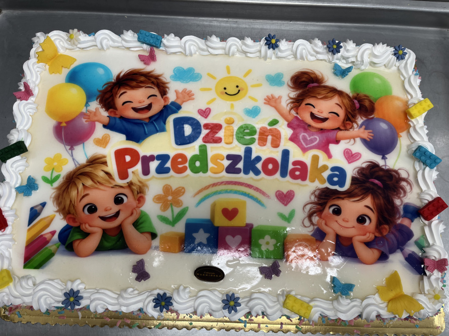 Tort z napisem „Dzień Przedszkolaka”, ozdobiony ilustracjami uśmiechniętych dzieci, kolorowych balonów, klocków, kwiatów i motyliTort z napisem „Dzień Przedszkolaka”, ozdobiony ilustracjami uśmiechniętych dzieci, kolorowych balonów, klocków, kwiatów i motyli