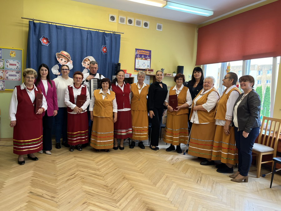 Członkowie zespołu warmińskiego w tradycyjnych strojach oraz zaproszeni goście pozują do wspólnego zdjęcia w sali przedszkolnej