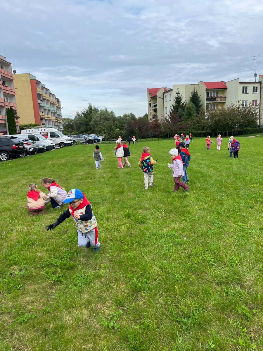 Dzieci w rękawiczkach zbierają śmieci na trawniku podczas akcji Sprzątanie świata ucząc się troski o czystość i środowisko